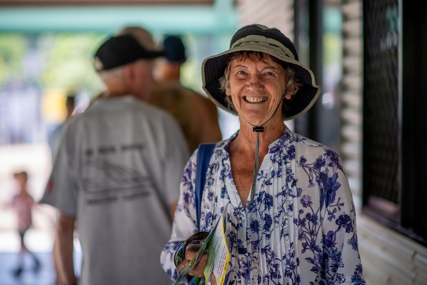 An older woman wearing a bucket hate and holding pamphlets, smiling