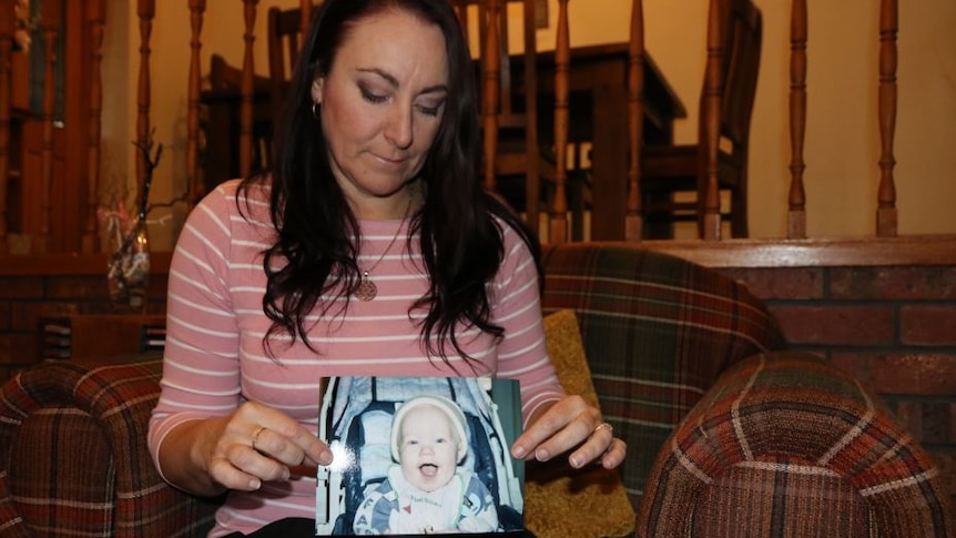A lady sits down holding a photo of her baby