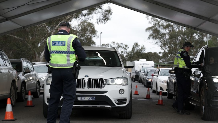 A police officer standing in front of a white four-wheel-drive with cars lined up behind it