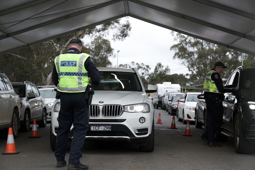 A police officer standing in front of a white four-wheel-drive with cars lined up behind it