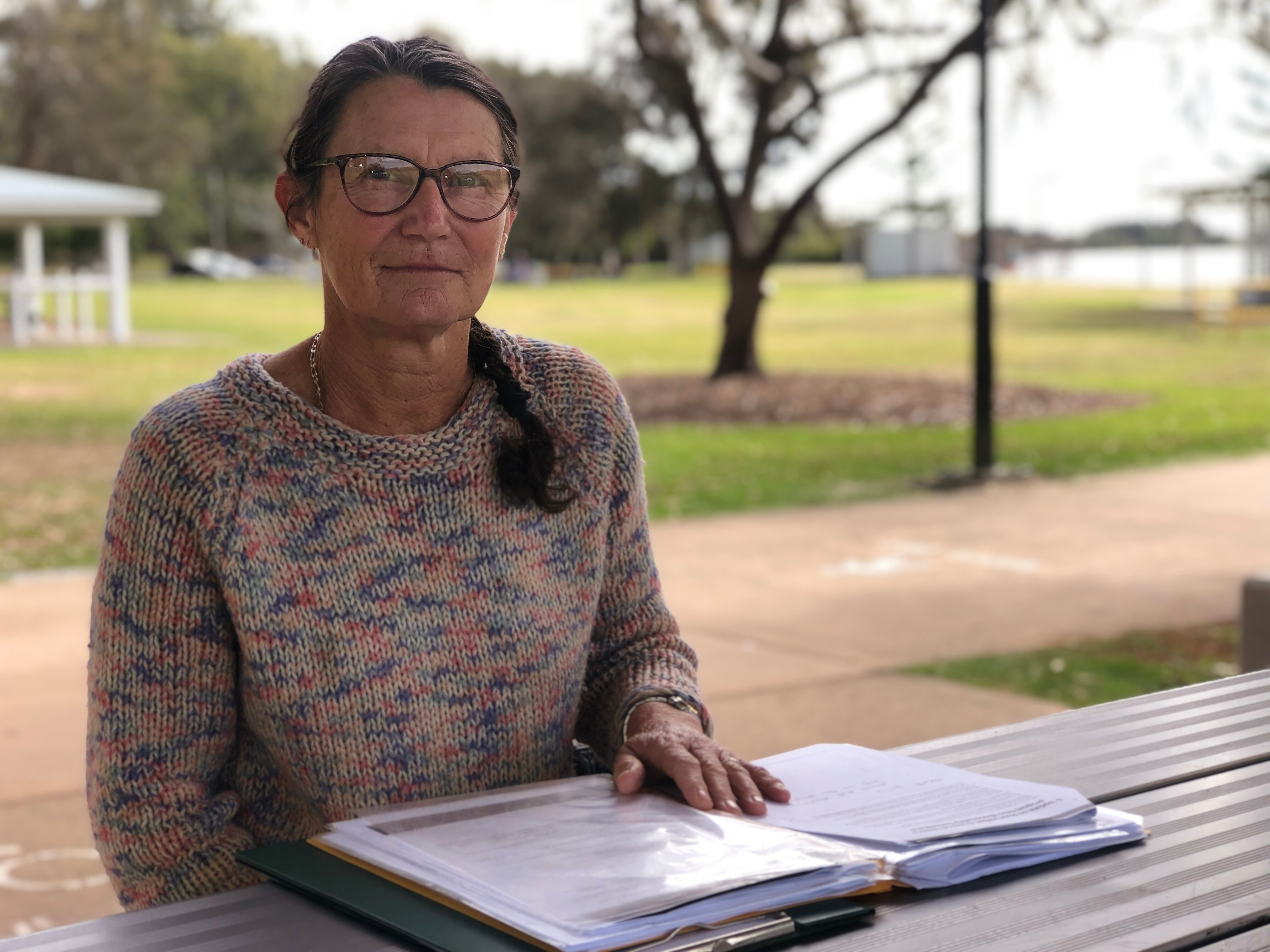 A concerned looking lady sitting at a picnic table with all the paperwork she has collected on the program ending.