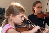 8yo girl in pink top concentrates as she plays violin next to woman in black top also playing violin