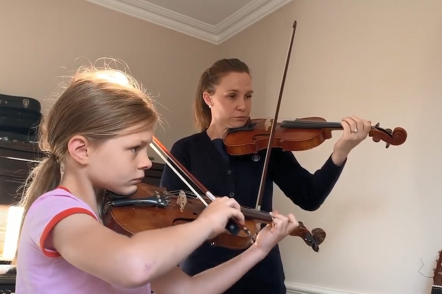 8yo girl in pink top concentrates as she plays violin next to woman in black top also playing violin
