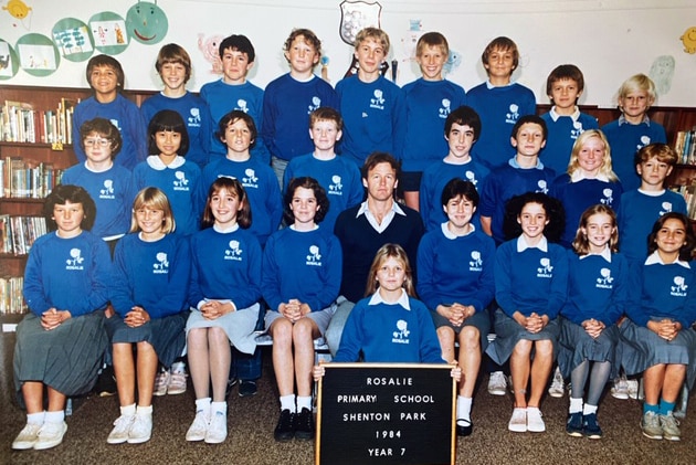 A group of children in school uniforms pose in rows.