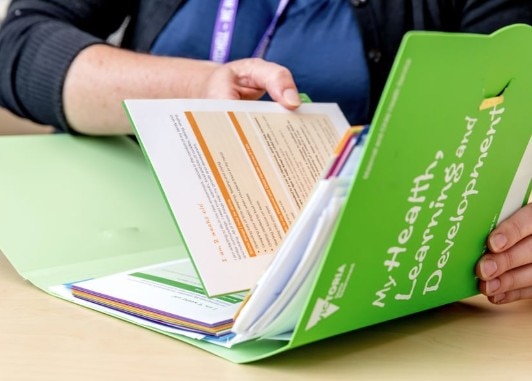 A person's hands take a piece of paper out of a green book