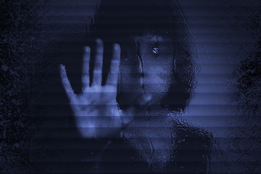 A blurred, dark photo of a child holding her hand up behind a glass screen.