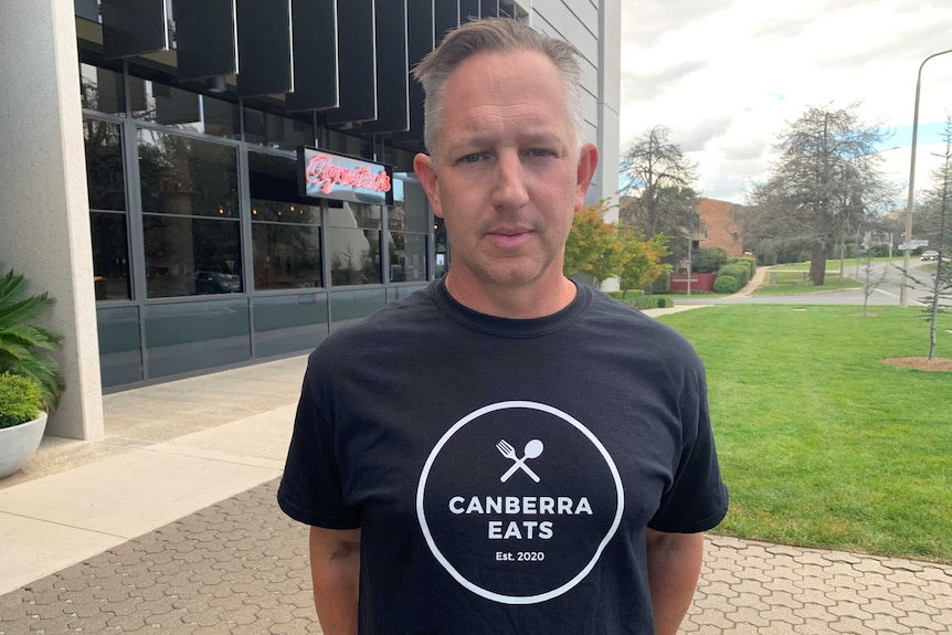 A grey-haired man wears a black t-shirt which says 'Canberra Eats'