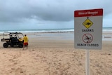 A surf patrol buggy with a surf life saver on a beach, with a sign that reads "beach closed" and "sharks".