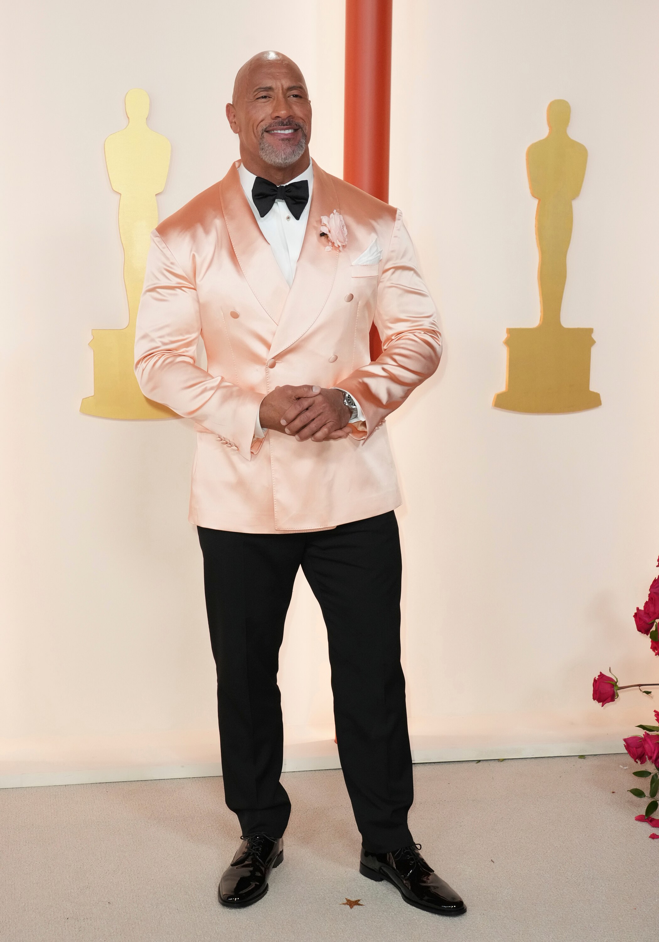 Dwayne Johnson wearing a silky pale pink suit jacket, a black bow tie and black trousers