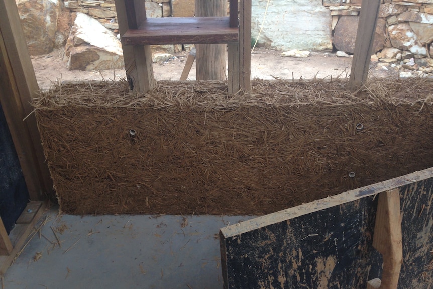 A photo of a wooden frame of a house, when straw was being added as insulation