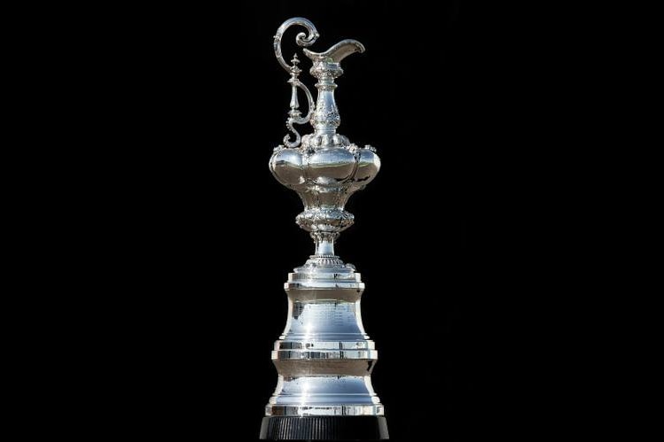A long, slim, ornate and old fashioned silver trophy gleams in front of a black background.