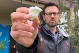 A man standing in front of an apartment holding a piece of polystyrene foam towards the camera.