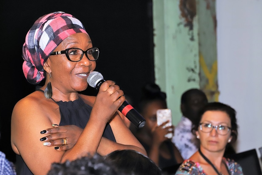 An African Australian woman in a bandana speaks into a mike.