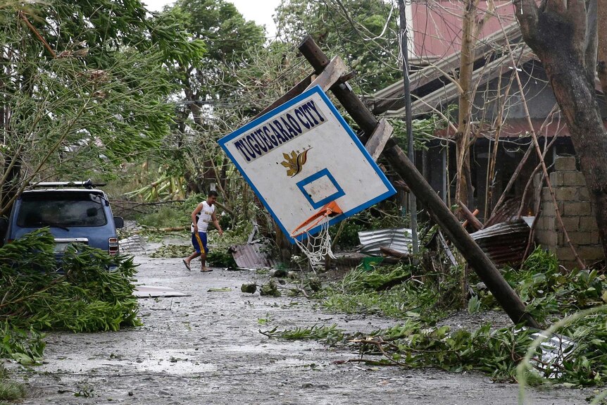 A resident walks beside toppled trees and a basketball hoop