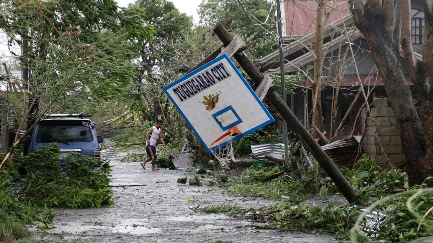 A resident walks beside toppled trees and a basketball hoop