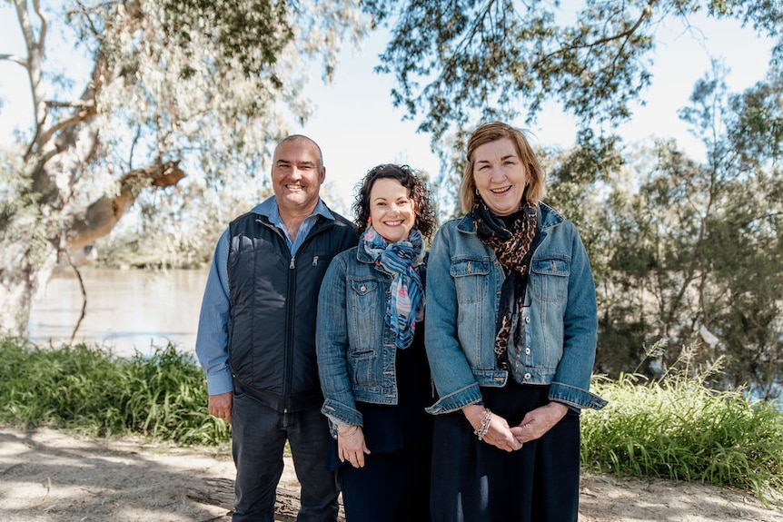 Three people standing in front of a river smiling at camera. 