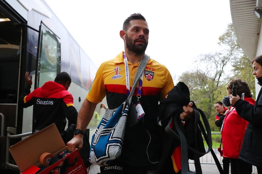 A man stepping off a bus wearing a rugby jersey and with a large blue and silver PNG bilum bag slung over his body. 