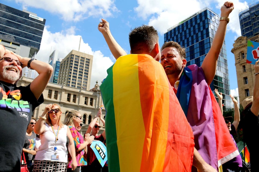 In a large crowd, two men prepare to hug after hearing the result of the postal survey