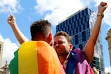 In a large crowd, two men prepare to hug after hearing the result of the postal survey