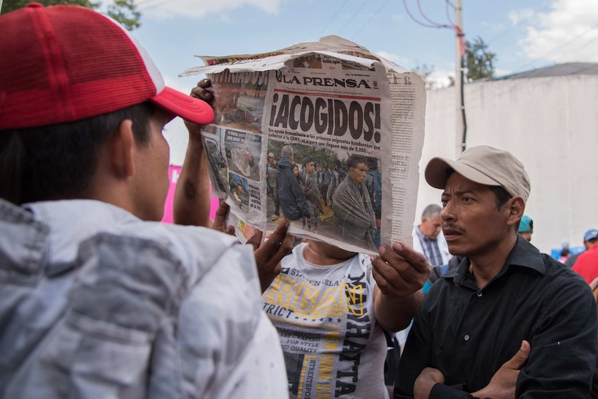 People from the migrant caravan look at a Mexican newspaper