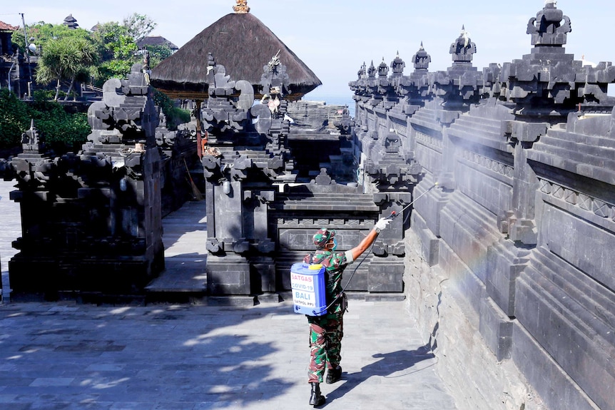 A man in army fatigues sprays a mist on a temple wall