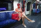 A woman in a facemask and hat sits on the London tube