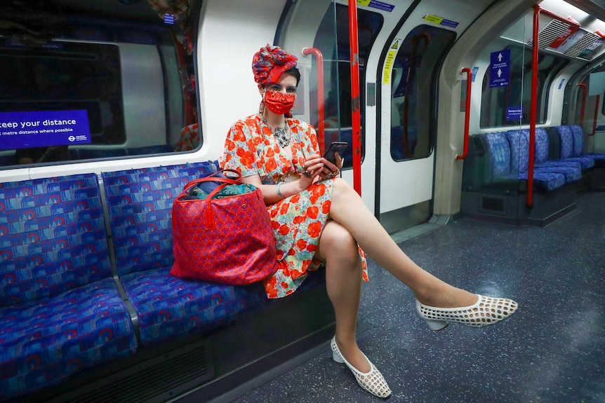 A woman in a facemask and hat sits on the London tube