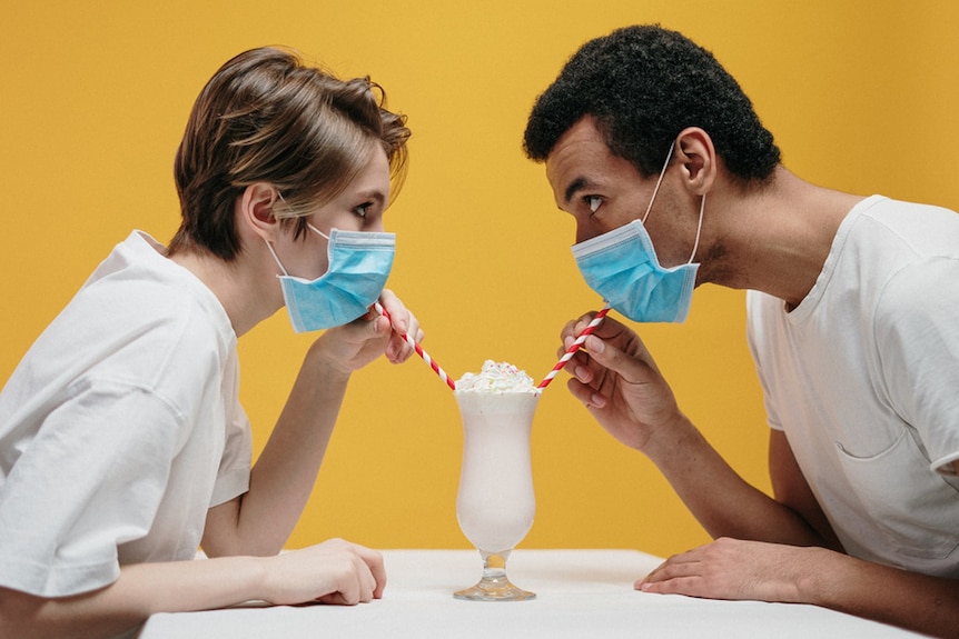 A couple wearing protective masks share a milkshake