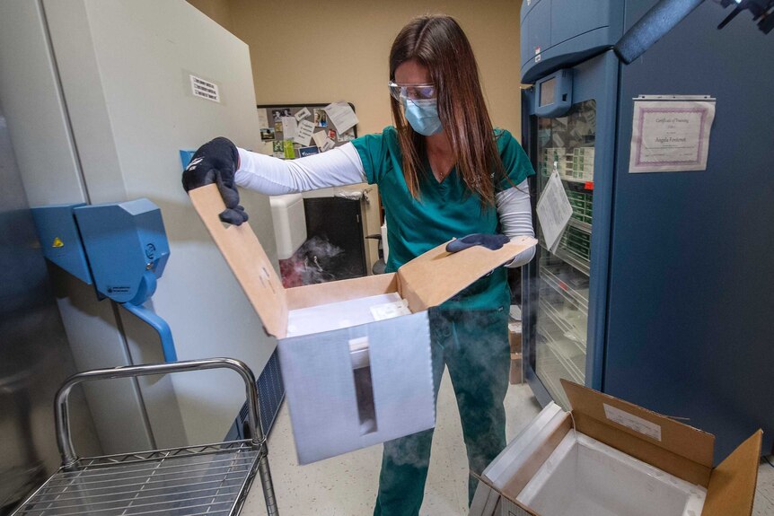 A woman in scrubs and a face mask opens a box