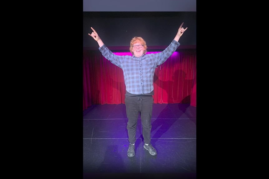 young boy stands on stage with his hands in the air celebrating after his comedy performance. 