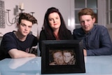 Three family members sit behind photo of the late father.