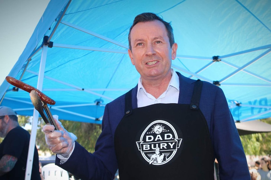 Premier Mark McGowan holds up a sausage with a tong