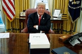 Donald Trump sits at his desk in the Oval Office with his arms crossed.