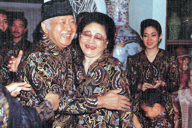 Man wearing batik smiling while hugging a woman wearing same  outfit.