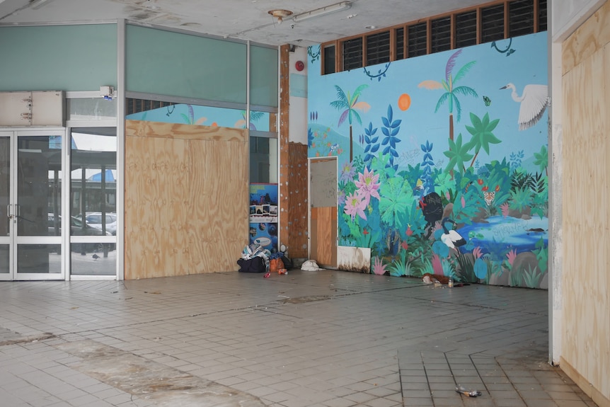 Bags and rubbish sit outside a wooden board, next to another wall of artwork covered in graffiti