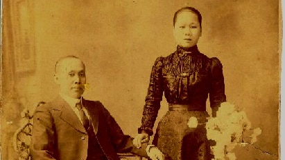 An old photograph of a man in a suit and a woman in a high-necked blouse holding a bunch of flowers