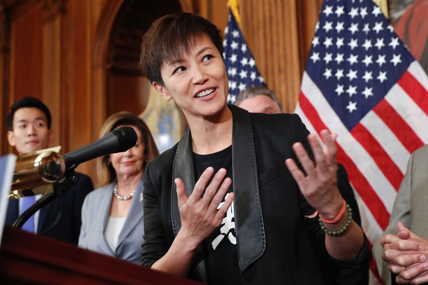 Hong Kong activist Denise Ho speaks at a podium while several US congress members stand behind her