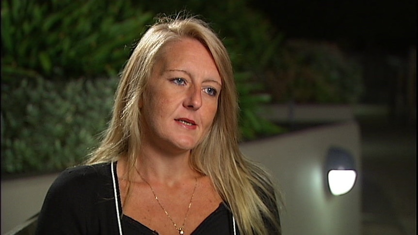 A blonde woman wearing black talks to a camera.