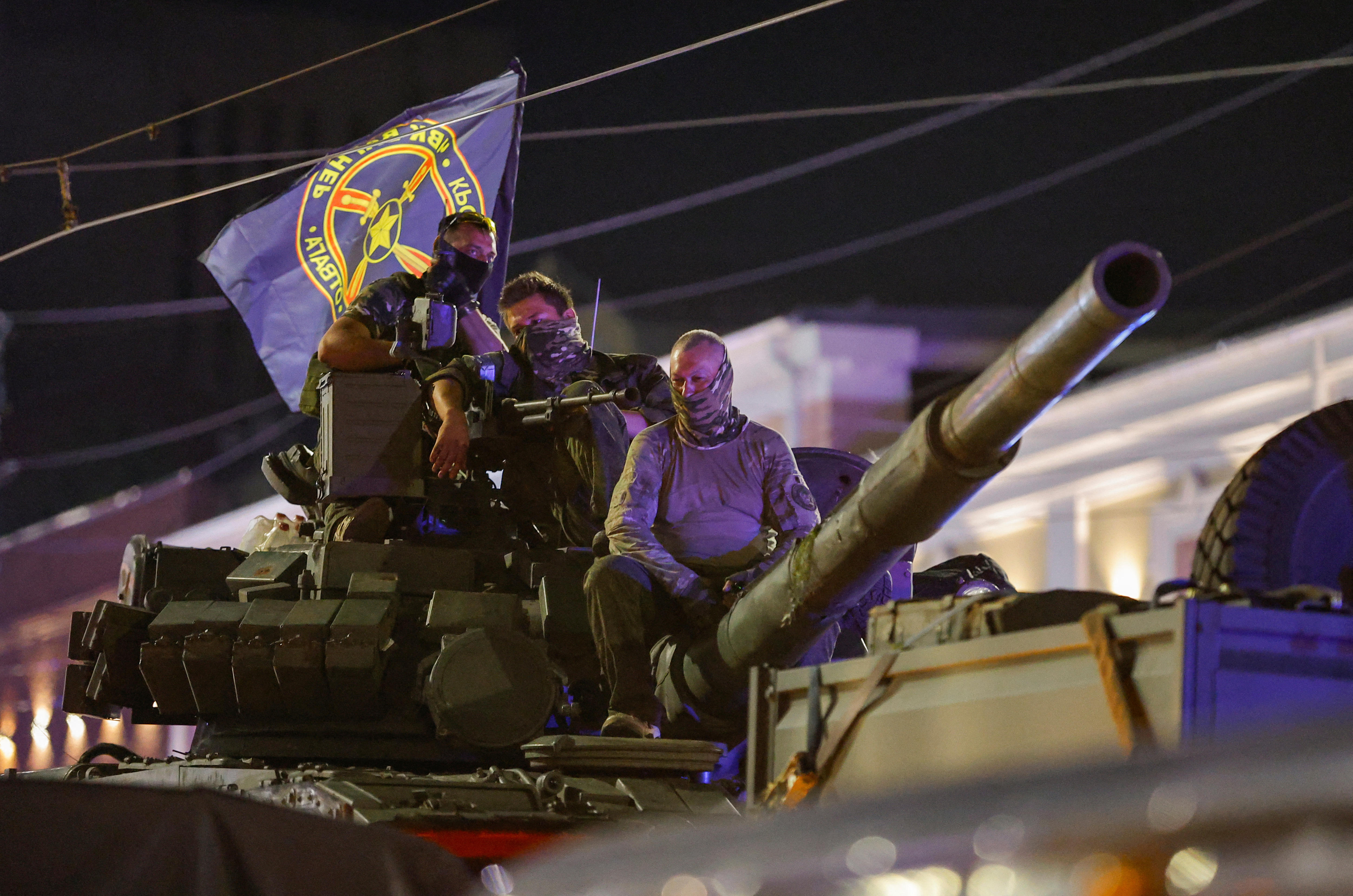 Wagner mercenary fighters on top of a tank, with a Wagner flag.