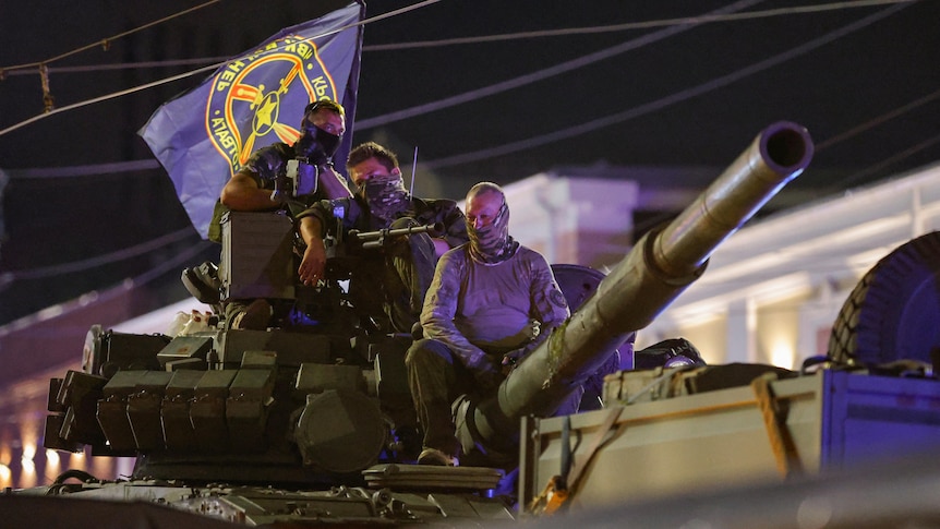 Wagner mercenary fighters on top of a tank, with a Wagner flag.