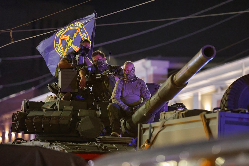 Wagner mercenary fighters on top of a tank, with a Wagner flag.