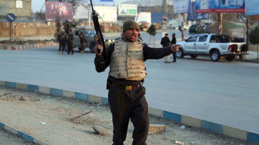 A Afghan security force member is wearing a bullet-proof vest and holding a gun in the middle of a street
