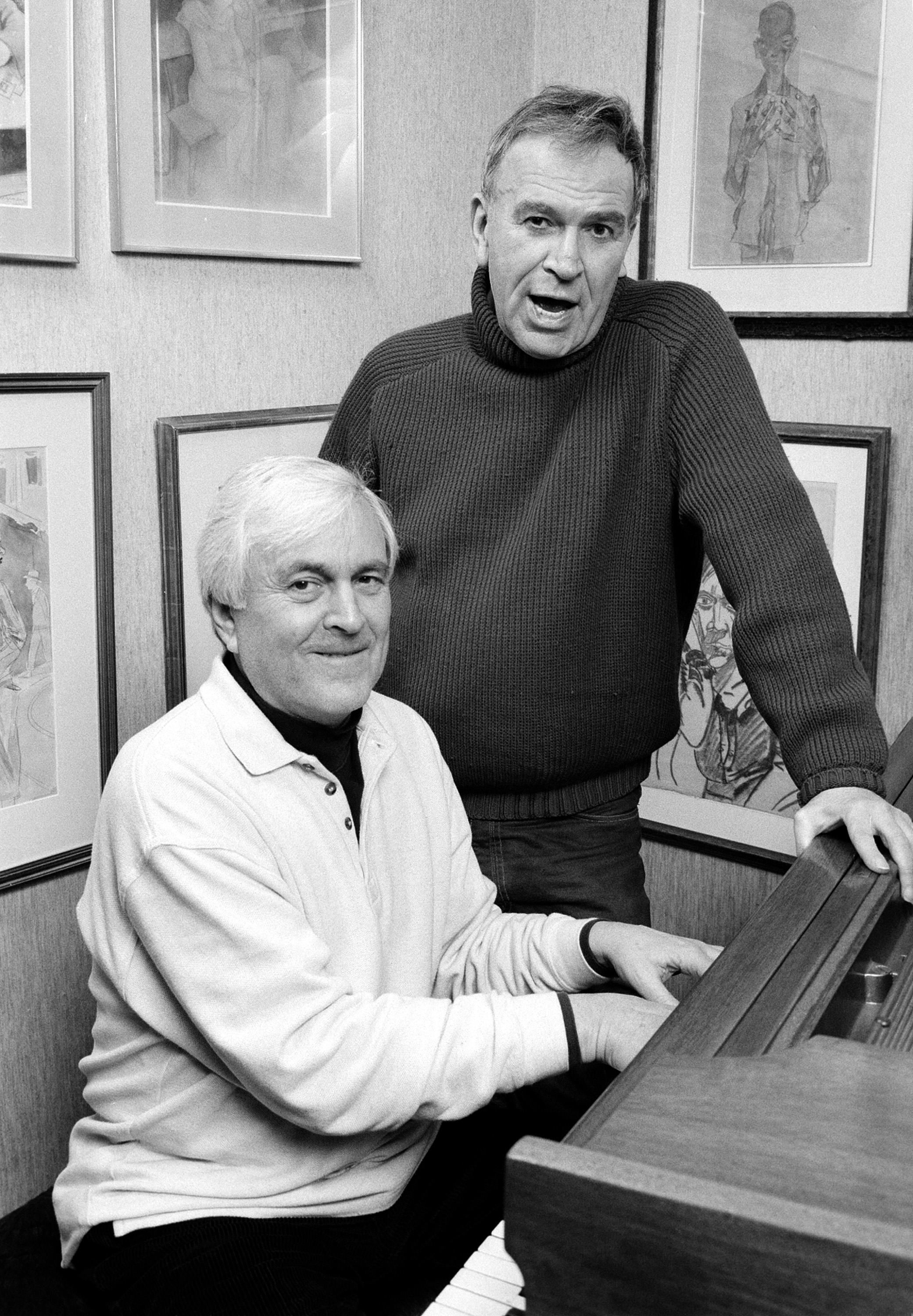 A black and white photo of John Kander and Fred Ebb rehearsing at a piano in Ebb's apartment in 1991.