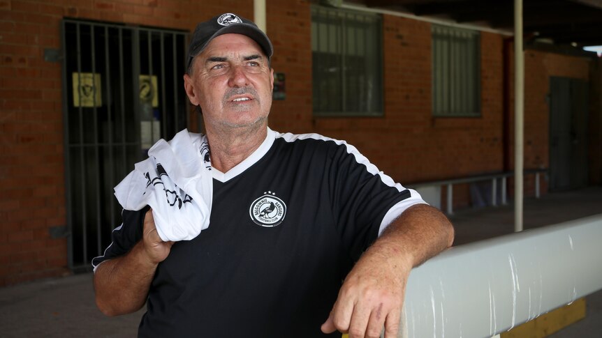 Steve Buckley wears a black soccer shirt and hat with a white shirt over his shoulder, looking off camera.