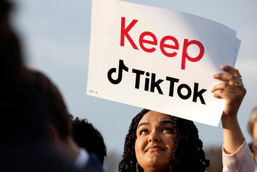 A woman holds up a sign reading 'keep tiktok' 