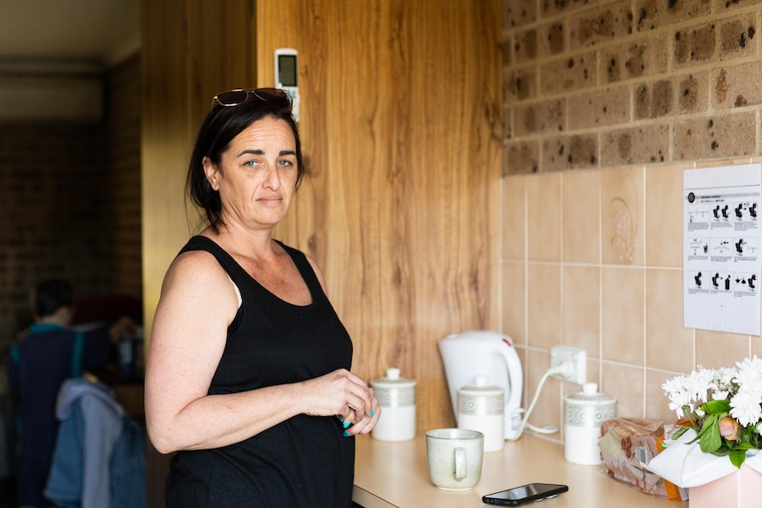 A lady with black hair stands in the kitchen of her motel