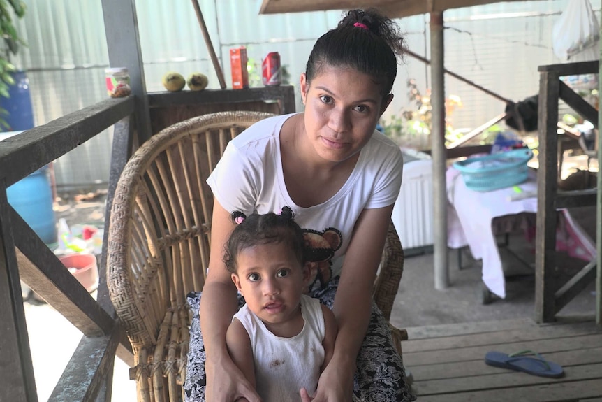 Woman sitting in chair holds arms of daughter at her feet.