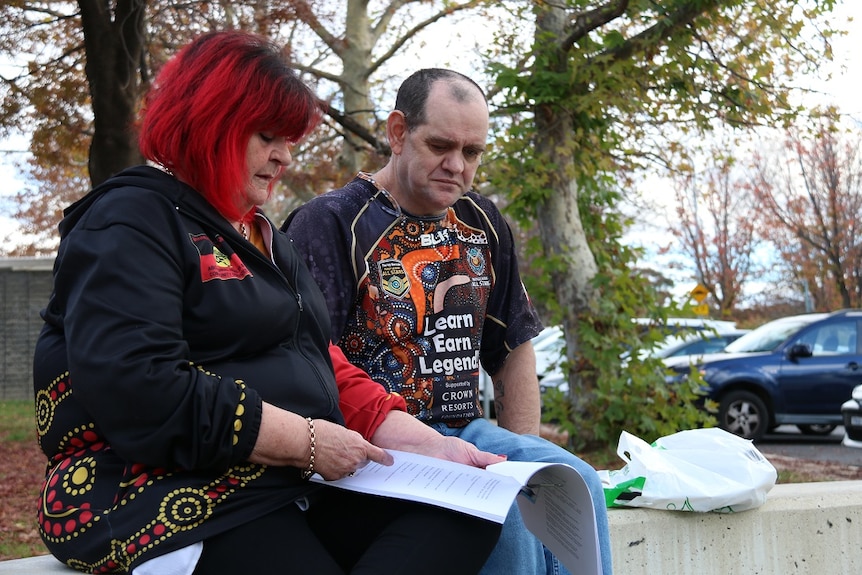 A man and a man sit in a concrete wall, reading over some documents.