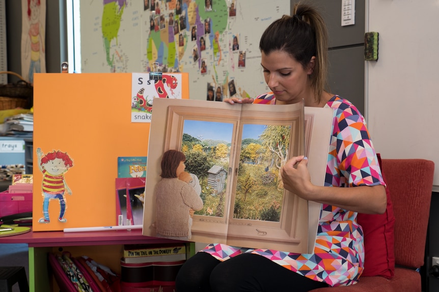 Ms Camporeale sits and reads a story book.