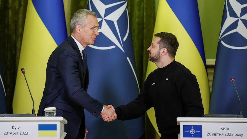 NATO leader and Zelenskyy shake hands in front of the Ukraine and NATO flags at a conference.